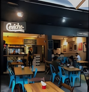 A restaurant with a sign reading "Cerviche". Inside, there are tables and chairs, and a person is visible in the background. - Perto da Praia - Botafogo - HOTSPOT (Rio de Janeiro)