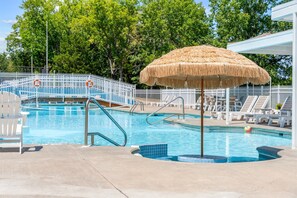 Ein Swimmingpool mit einem Reetdachschirm, Liegestühlen und einem weißen Zaun.