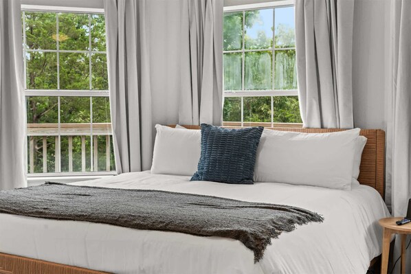 Uma cama com roupa de cama branca, um travesseiro azul escuro e um cobertor cinzento.