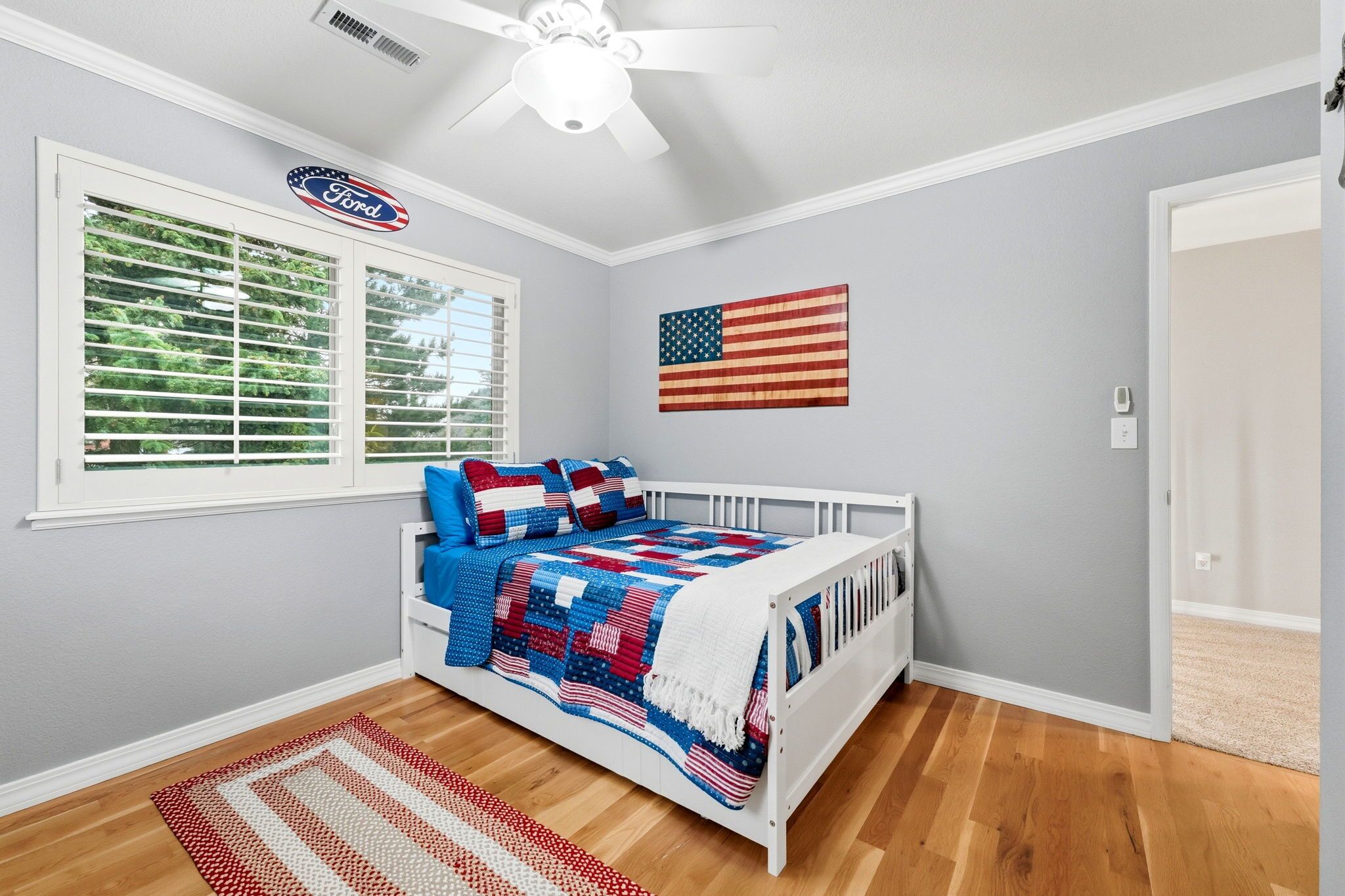 Ein Schlafzimmer mit einem weißen Bett, einer Dekoration mit der amerikanischen Flagge und dem Ford-Logo am Fenster.