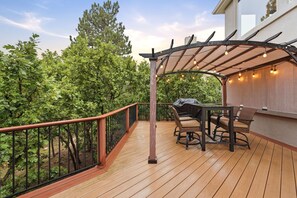 Eine Holzterrasse mit einer Pergola, Sitzgelegenheiten im Freien und Blick auf eine bewaldete Gegend.