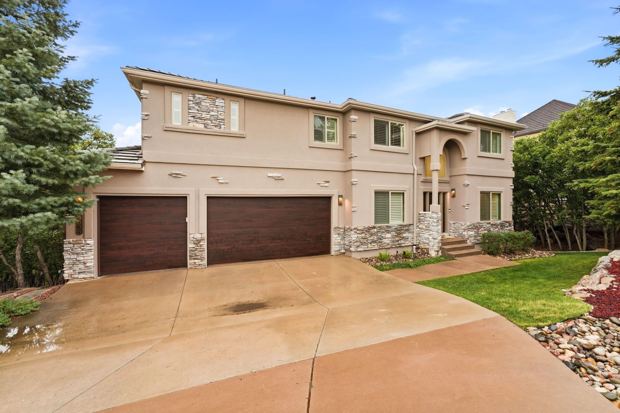 A two-story house with a stone facade, two garage doors, and a well-maintained lawn.