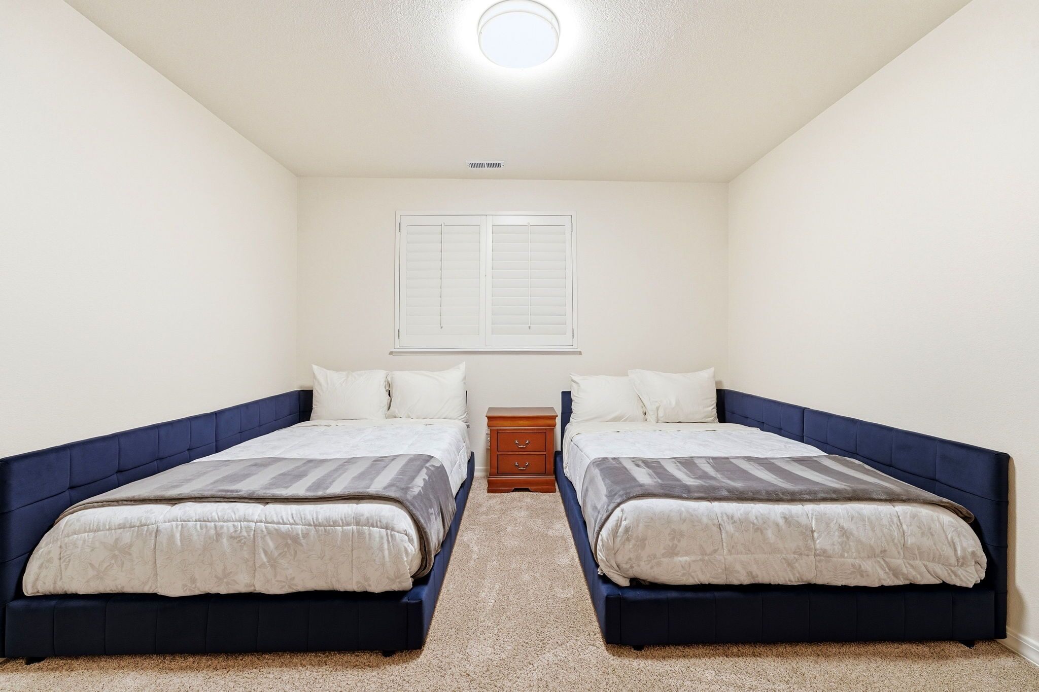 A bedroom with two beds, a nightstand, and a window with blinds.