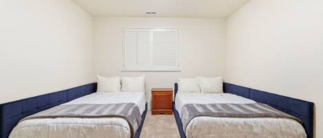 A bedroom with two beds, a nightstand, and a window with blinds.