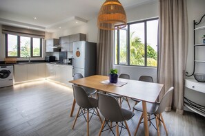 A modern kitchen with a dining area, large windows, and a view of greenery. - Cozy 2-bedroom apartment in peaceful Pereybere (Grand Baie)