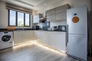 A modern kitchen with a built-in washing machine, a large refrigerator, and a window with a view of greenery. - Cozy 2-bedroom apartment in peaceful Pereybere (Grand Baie)