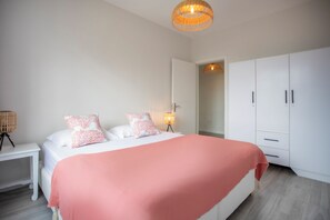 Une chambre à coucher avec un lit, une armoire blanche, une lampe de chevet et un luminaire au plafond.
