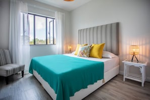 A bedroom with a bed, a chair, a bedside table, and a window. - Cozy 2-bedroom apartment in peaceful Pereybere (Grand Baie)