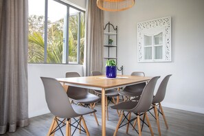 A dining area with a wooden table and six chairs, a potted plant, and a window with curtains. - Cozy 2-bedroom apartment in peaceful Pereybere (Grand Baie)