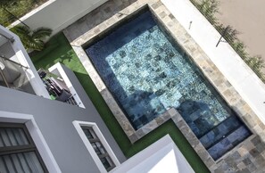 A swimming pool with a stone border, surrounded by a white building and a green lawn. - Cozy 2-bedroom apartment in peaceful Pereybere (Grand Baie)