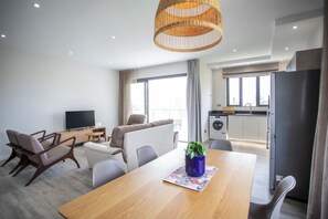 A modern living room with a wooden dining table, a sofa, and a television. - Cozy 2-bedroom apartment in peaceful Pereybere (Grand Baie)