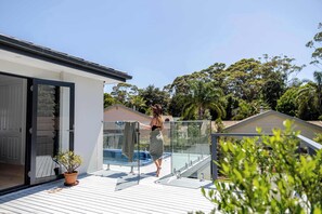 Ein modernes Haus mit einem Glasbalkon, einem Swimmingpool und einem Garten.