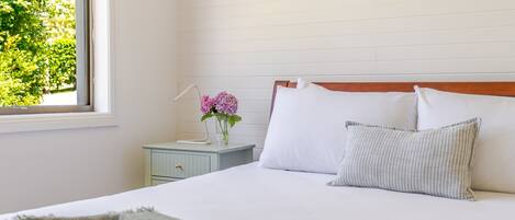 A bedroom with a bed, a nightstand, a window, and a view of greenery outside.