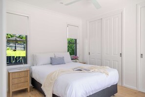 Un dormitorio con cama, mesitas de noche, un ventanal con vistas a un jardín y una puerta.