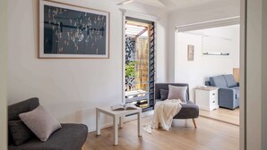 Una sala de estar moderna con ventilador de techo, un cuadro abstracto grande y vista a un jardín a través de una puerta de cristal.