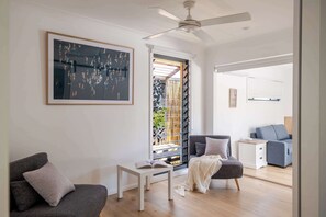 Ein modernes Wohnzimmer mit Deckenventilator, einem großen abstrakten Gemälde und Blick auf einen Garten durch eine Glastür.