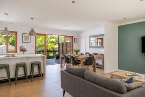 A modern kitchen with a dining area, bar stools, and a grey sofa. - Summer and Winter by The Sea - Outdoor Spa (Mollymook Beach)