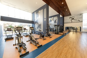 A gym with various exercise equipment, large windows, and a wooden floor.