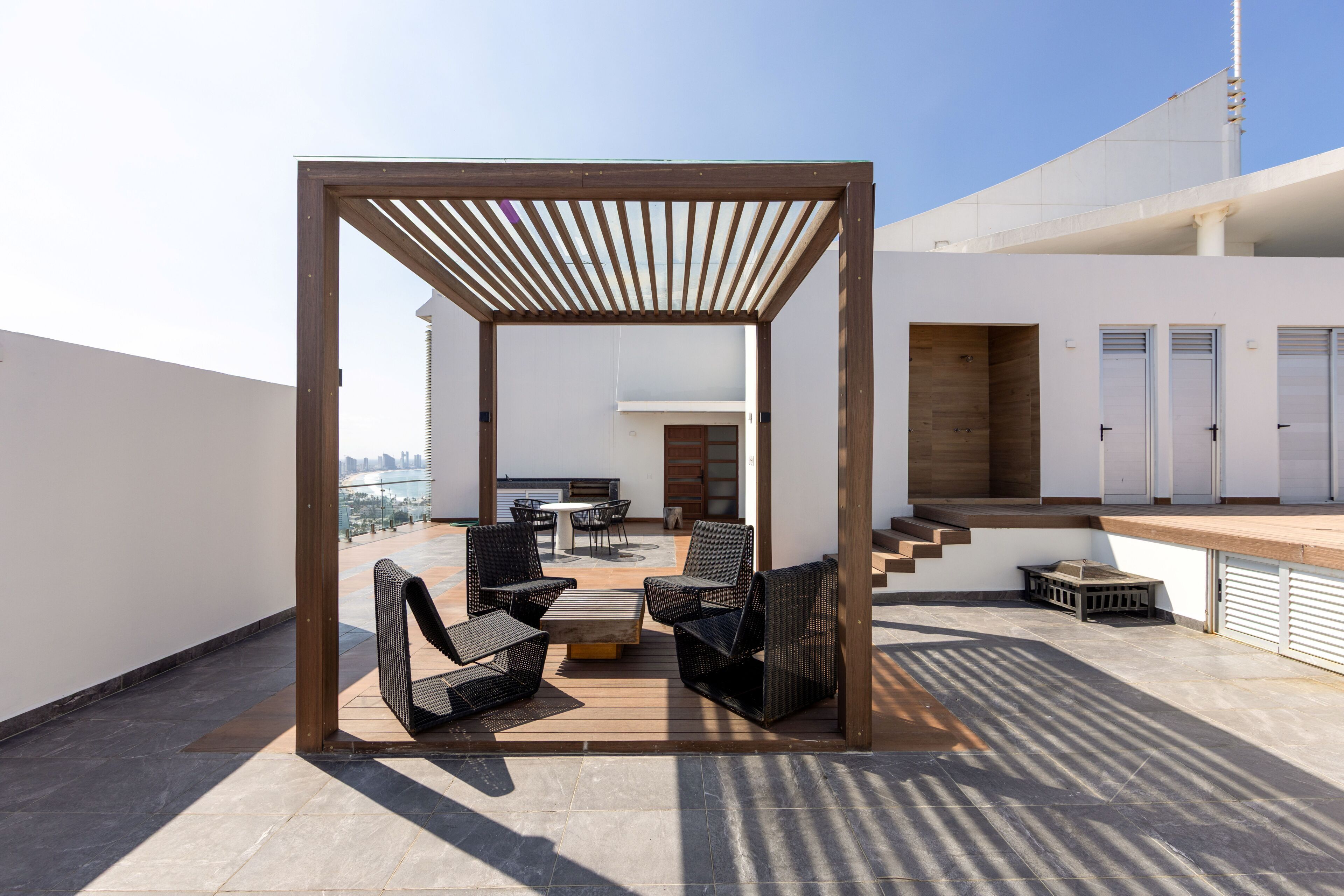 Terraço no telhado com pérgula de madeira, mobiliário de exterior e vista para o horizonte da cidade.