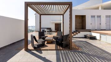 Terraço no telhado com pérgula de madeira, mobiliário de exterior e vista para o horizonte da cidade.