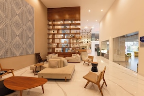 Un hall d’entrée spacieux au design moderne, comprenant un grand espace de détente avec des canapés et des fauteuils, une bibliothèque en bois et une grande œuvre d’art abstraite murale.