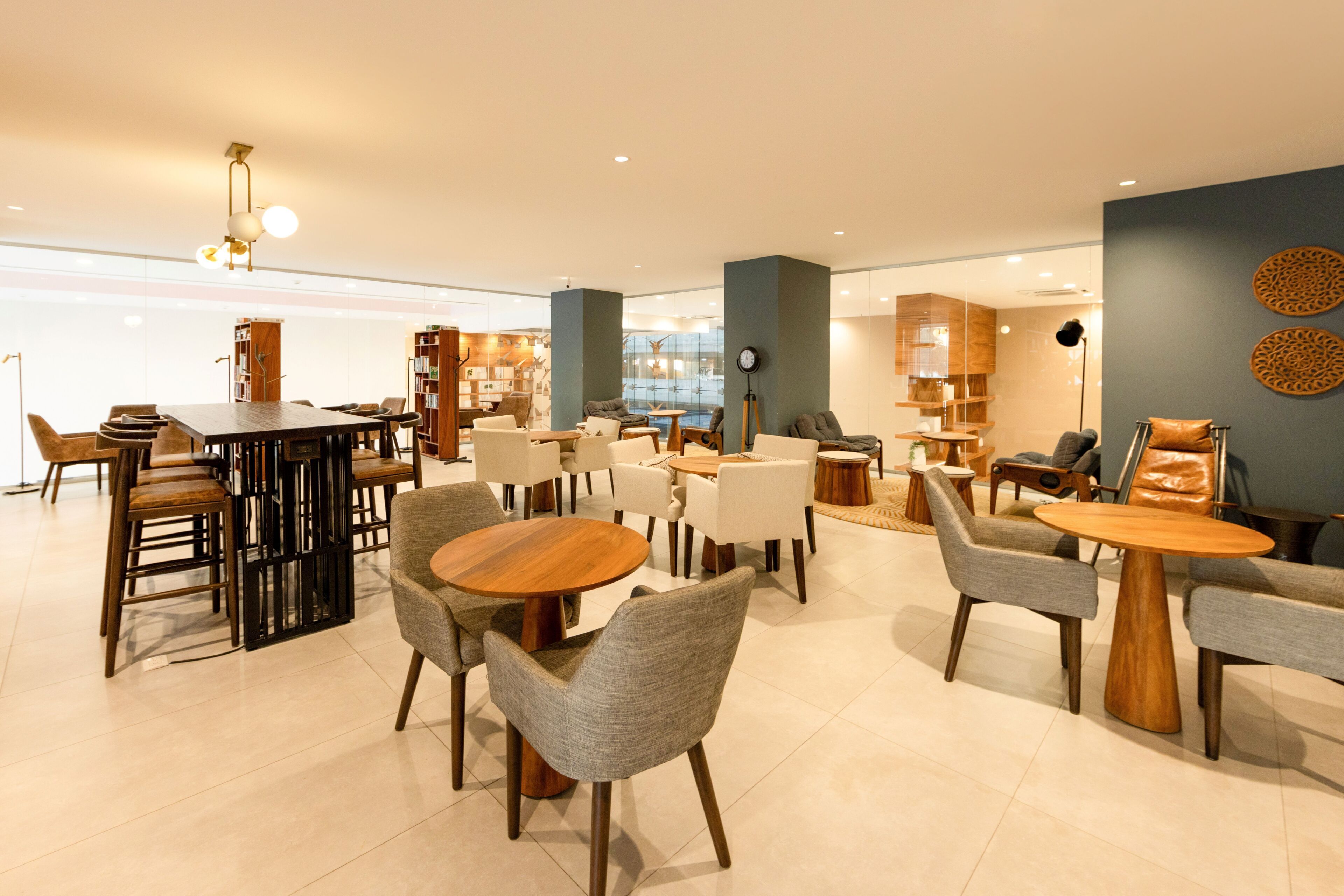 Um interior moderno com mesas e cadeiras redondas, um bar e uma área de estar com estantes.