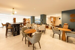 Un intérieur moderne avec des tables et des chaises rondes, un coin bar et un espace salon agrémenté d’étagères à livres.