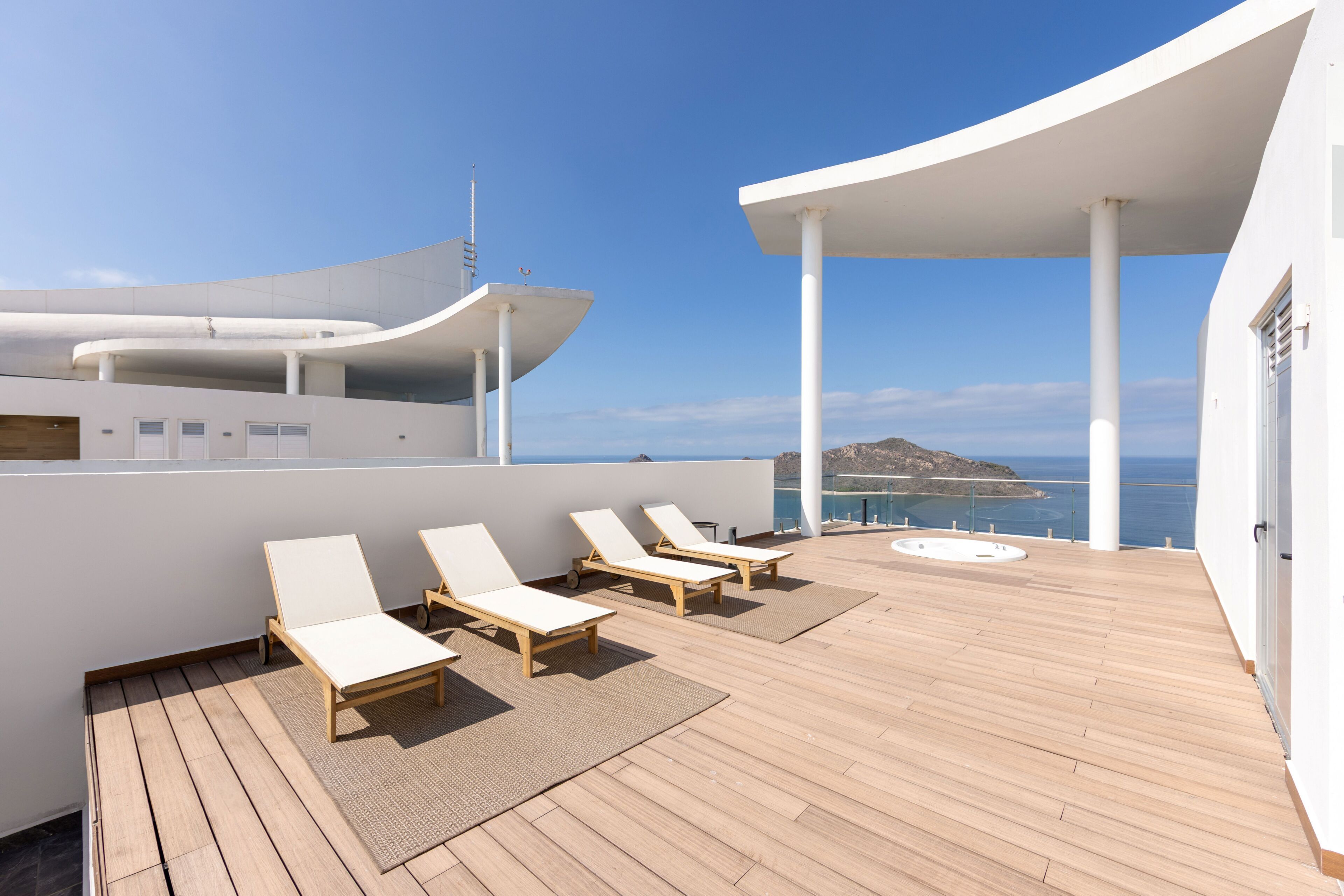 A deck with sun loungers and a hot tub, overlooking a body of water and a distant island.