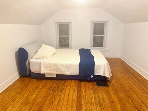 A small, single-bed room with a sloped ceiling, white walls, and wooden flooring.