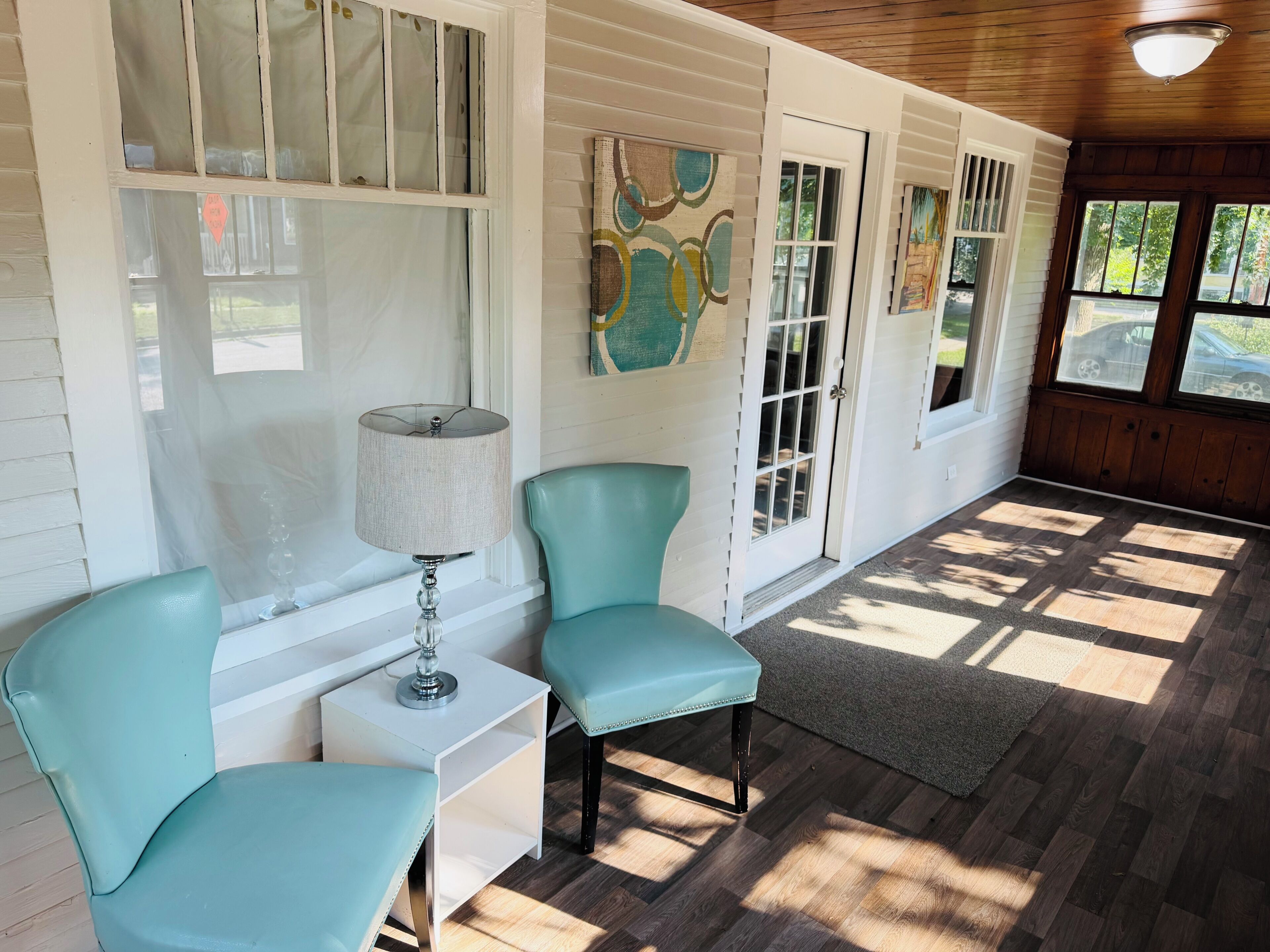 A room with two teal chairs, a table with a lamp, and artwork on the walls.