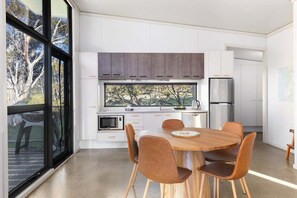 Une cuisine moderne avec des meubles blancs, un réfrigérateur en acier inoxydable et un coin repas comprenant une table et des chaises en bois.