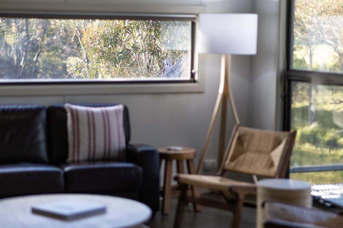 Et værelse med en sofa, en lænestol, en lampe og udsigt til træer gennem et vindue.