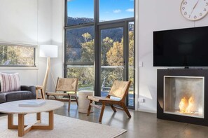 Un salon moderne doté d’une cheminée, de grandes fenêtres, d’un téléviseur à écran plat et de sièges confortables.
