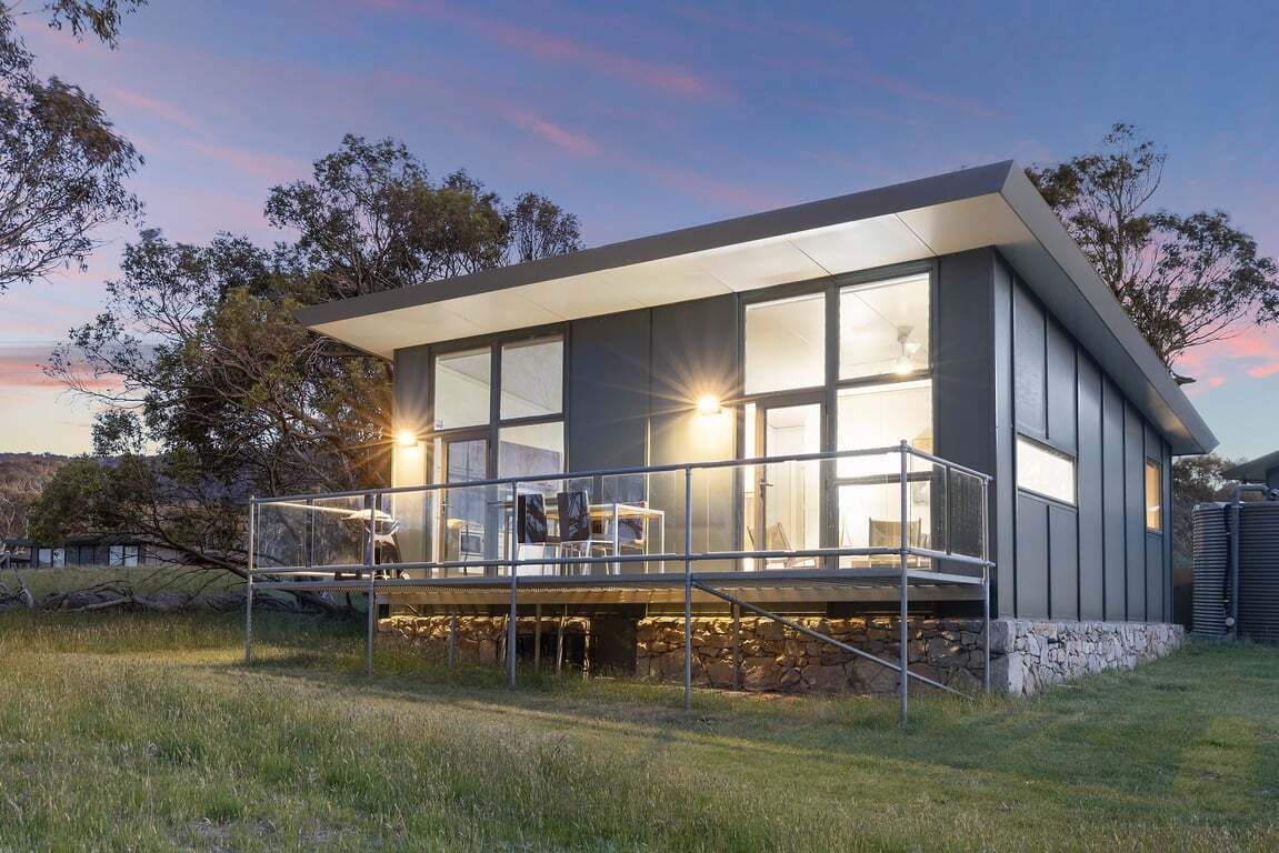 Une maison moderne dotée de grandes fenêtres, d’un espace extérieur couvert et de fondations en pierre.