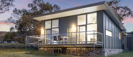 A modern house with large windows, a covered outdoor area, and a stone foundation.
