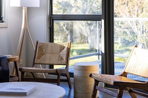 A room with a large window, two wicker chairs, a round table, and a lamp.