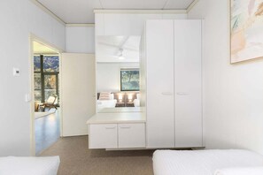 A hotel room with a large wardrobe, a bed, a seating area with a chair, and a view through a window.