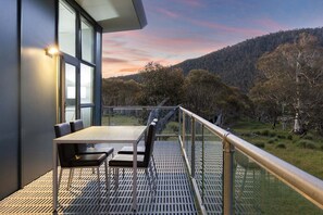 A modern outdoor seating area with a table and chairs, overlooking a hilly landscape. - Alpine Skye (Crackenback)