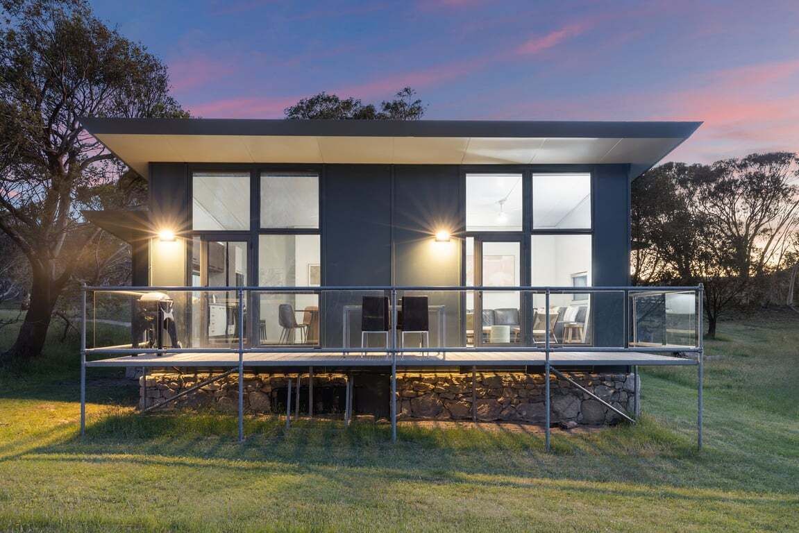 Een modern huis met een balkon, grote ramen en een stenen fundering.
