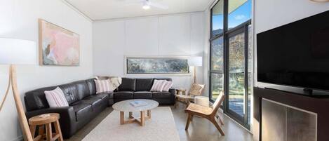 Una sala de estar moderna con un sofá de cuero negro, una mesa de centro redonda, una chimenea y ventanas amplias con vistas.