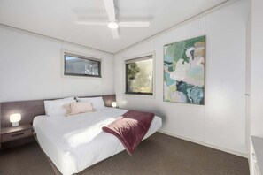 Ein modernes Schlafzimmer mit Bett, Nachttischlampen, Deckenventilator und Bildern an der Wand.