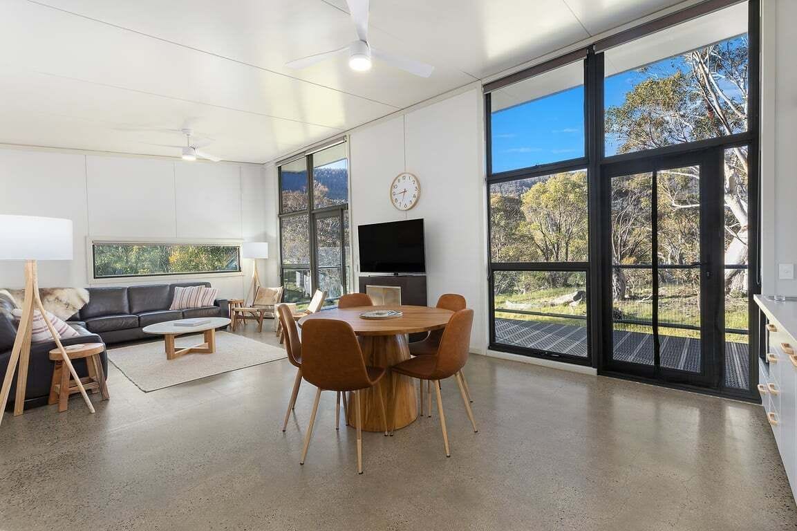 Uma sala de estar moderna com área de jantar, janelas amplas, televisão de tela plana e vista para o exterior.