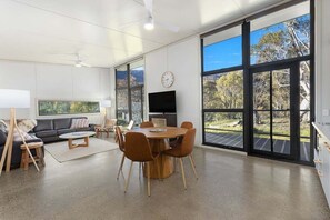 Ein modernes Wohnzimmer mit Essbereich, großen Fenstern, einem Flachbildfernseher und Blick ins Freie.