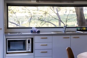 A kitchen with a built-in microwave, a sink, and a window overlooking a natural landscape. - Alpine Skye (Crackenback)