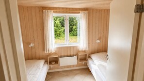 A small, cozy room with two single beds, a window with curtains, and a radiator under the window.