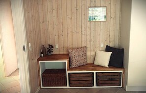 Eine Holzbank mit Stauraumschubladen und einem kleinen Regal, ein gerahmtes Bild an der Wand und ein Topfpflanze.