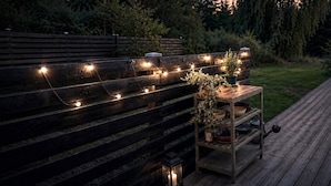Eine Holzterrasse mit Lichterketten und einem kleinen Tisch mit Topfpflanzen.