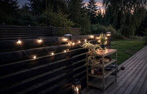 Eine Holzterrasse mit Lichterketten und einem kleinen Tisch mit Topfpflanzen.