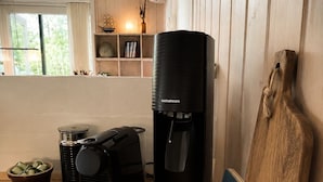Eine moderne Küche mit einer Kaffeemaschine, einem schwarzen Wasserspender und einem Schneidebrett, das an der Wand lehnt.
