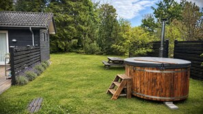 Ein Garten mit einem Whirlpool aus Holz, einer Holzterrasse und einem Picknicktisch.